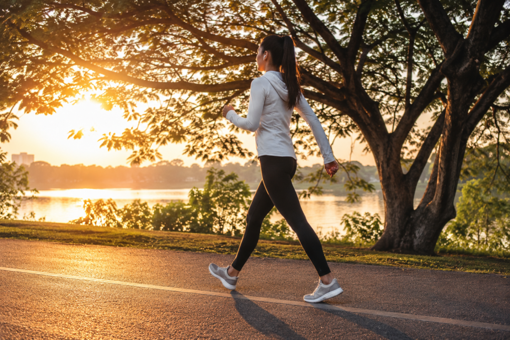 Como emagrecer com saúde. Foto inspiradora mostrando uma pessoa caminhando em um parque ao nascer do sol, vestindo roupas esportivas e transmitindo sensação de bem-estar e qualidade de vida.